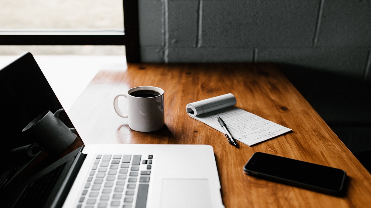 computer on a wooden table with a coffee mug and a notebook